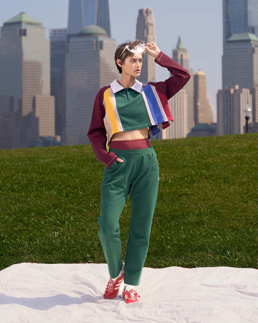 Brando Vassallo Editorial Fashion Lookbook Girl green pants with cropped rainbow stripe rugby shirt. hand in pocket and other hand on sunglasses. city skyline in background